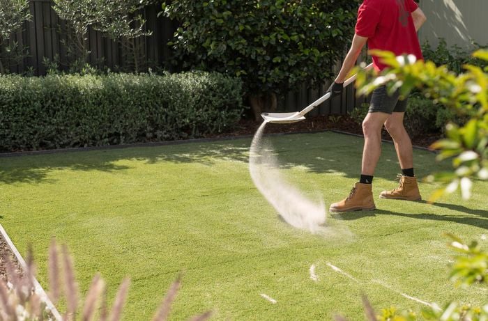 A person is spreading an even layer of synthetic turf sand over the turf using a shovel.