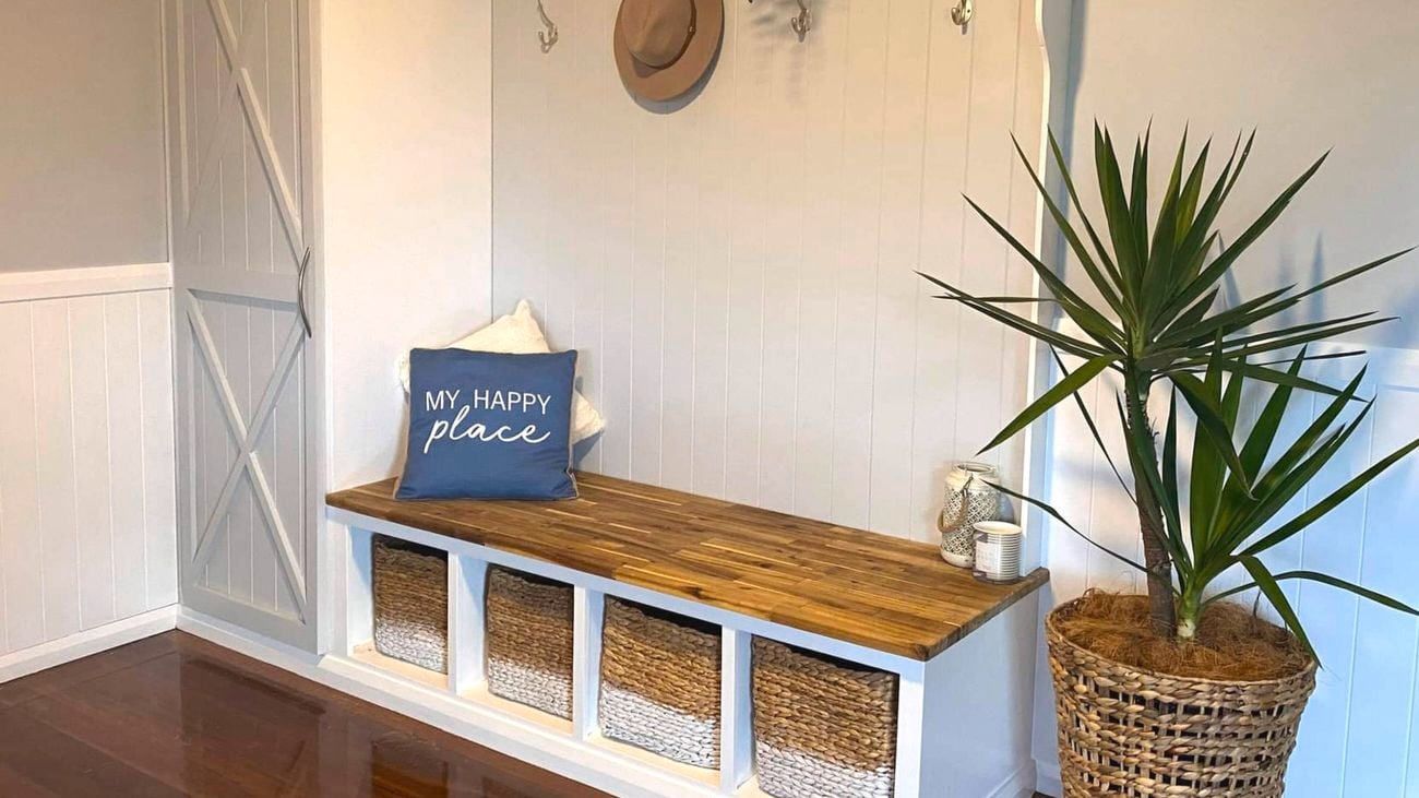 Mudroom bench with storage baskets, timber seat, wall hooks and a potted plant.