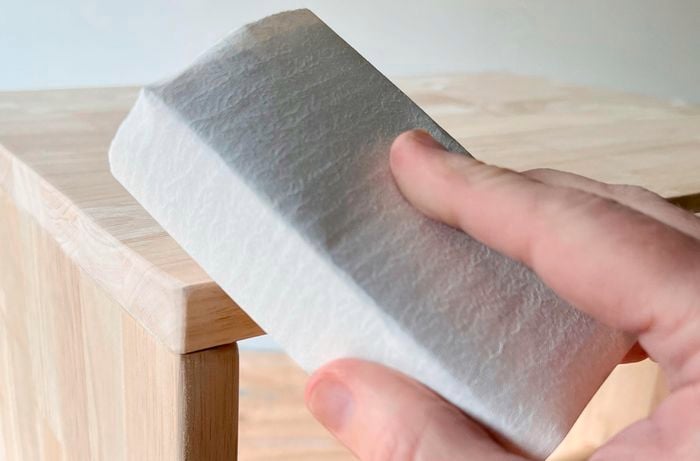 A person holding a sanding block against a timber piece