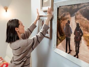 A woman standing in the foreground, mounting a painting on the wall. 