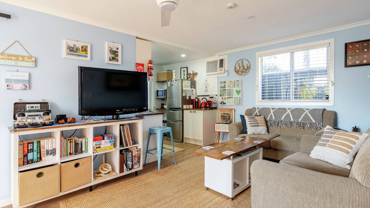 Interior view of a living room with light blue walls, a sofa, armchair, television on a shelving unit, and a small wooden coffee table.