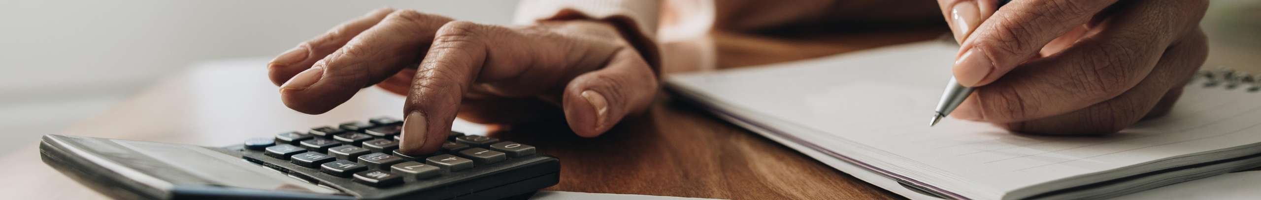 A woman calculating tax using a calculator, paper and pen.