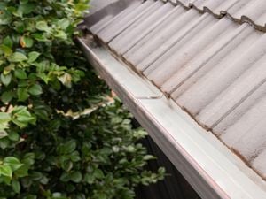 A freshly cleaned roof gutter along the edge of a house with grey tiled roofing