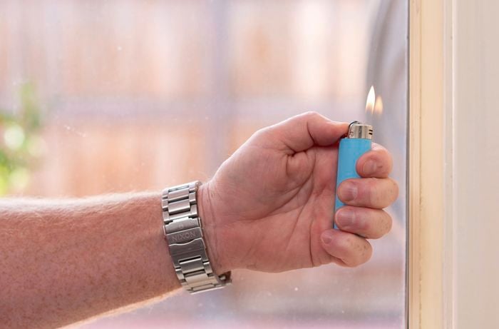 A hand holding a lighter with flames in front of the window.