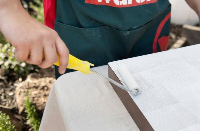 Person painting tabletop white with paint roller