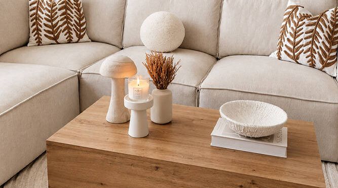 Coffee table styled with decorative vases, a candle and books in front of a cream modular sofa with patterned cushions.