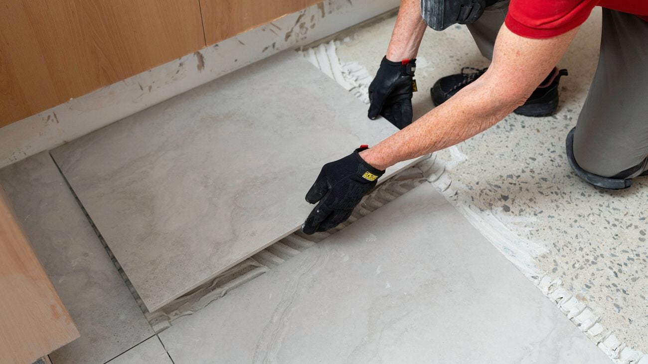 Gloved hands laying a large tile onto an adhesive bed.