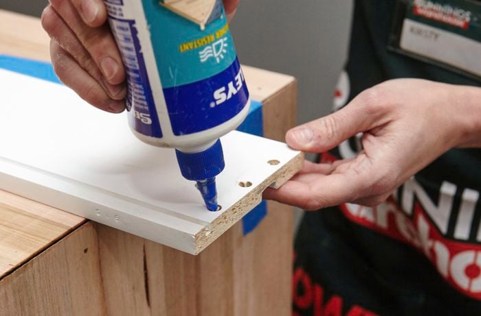 A person applying glue into the holes in a drawer panel