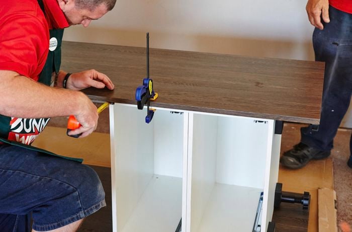 A person attaching a side panel to cabinets using a clamp