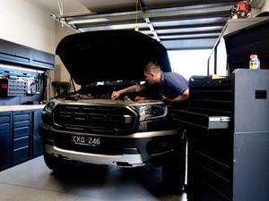 man fixing car in a garage with black tool workshop and tool box in the background