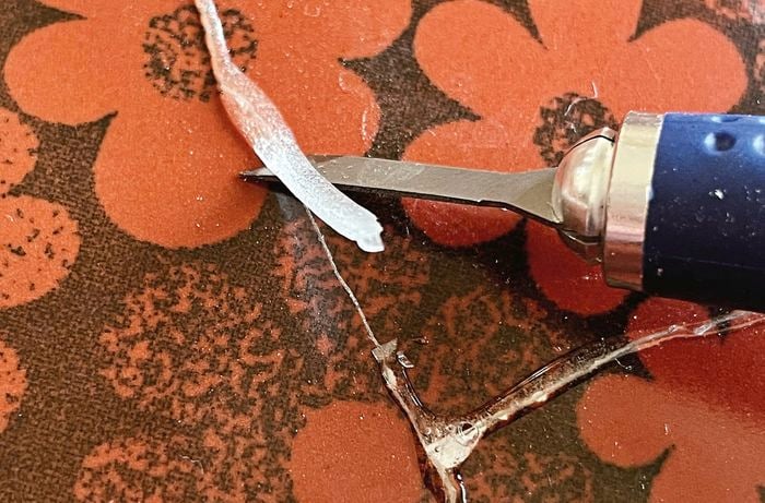 A craft knife is used to scrape off excess glue