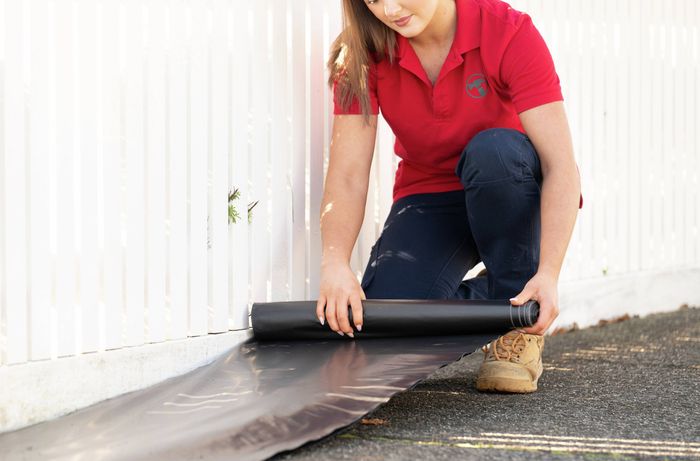 A Bunnings Team Member is preparing the area around fence before spray painting​​​   ​​​Image Description: A Bunnings Team Member is protecting surrounding surfaces with plastic sheeting before using a spray gun to paint a timber picket fence.