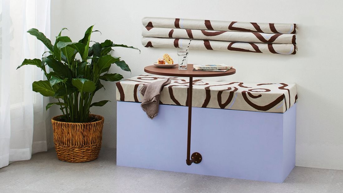 A cushioned bench seat with a ‘floating’ coffee table next to a green plant in a basket