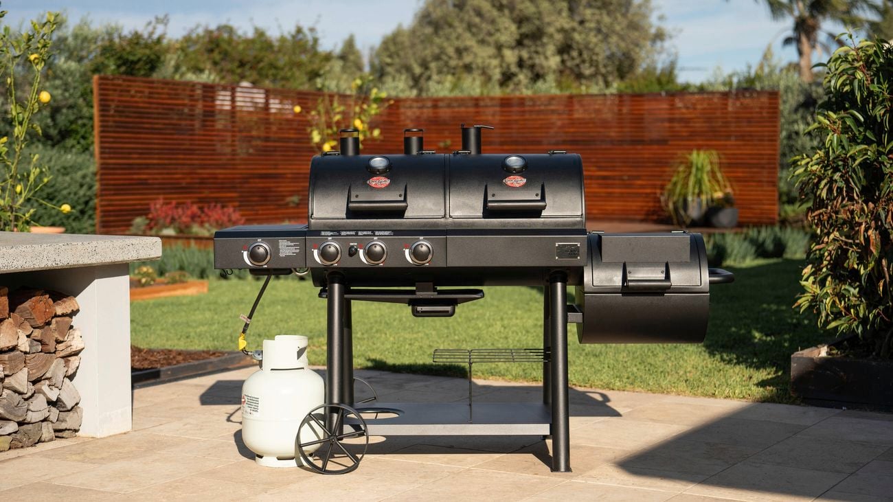 Char-Griller Texas Trio Gas and Charcoal Grill is placed on a patio in a landscaped backyard.