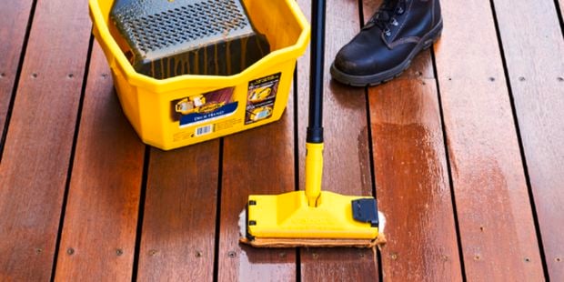 A person applying a decking product to a deck with the decking applicator and bucket