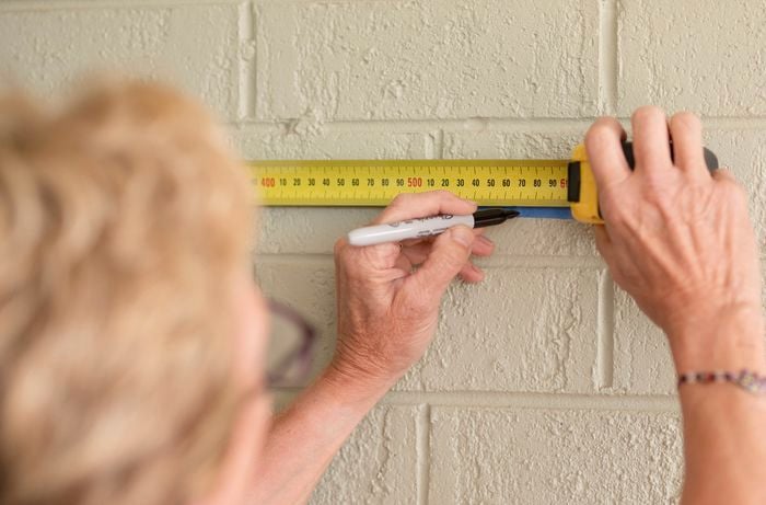 A person is marking the drilling spot on a brick wall with a tape measure