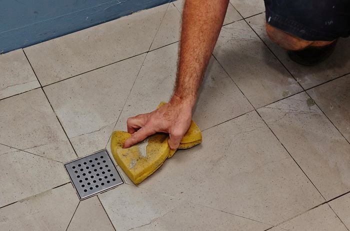 A person wiping tiles in a shower with a sponge