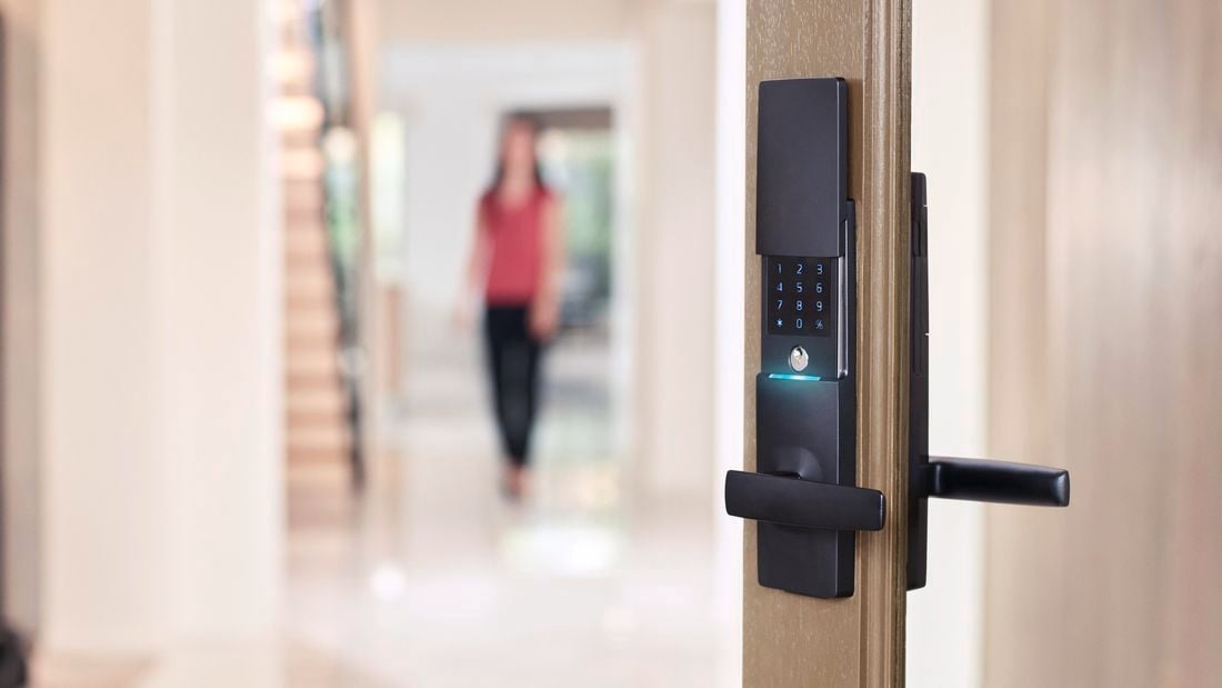 Close up of a black Gainsborough smart lock installed in a wooden-framed glass front door.