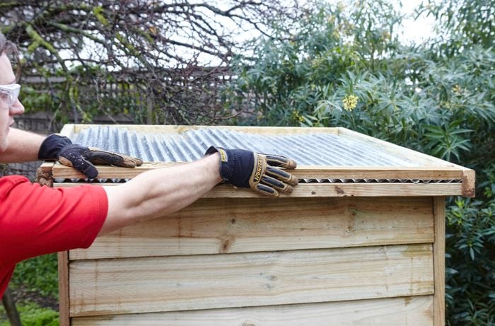 A corrugated iron roof being fitted to a chicken coop by a Bunnings team member, complete with leaf catcher