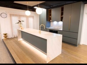 A modern green kitchen with a marble white benchtop and wooden floorboards.