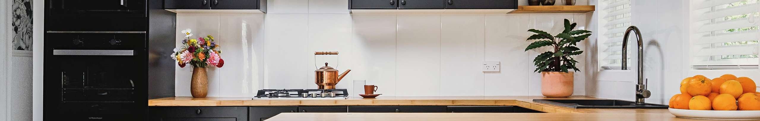 Kitchen with black cabinets and timber benchtops. Dining table with bench seat and cushions.