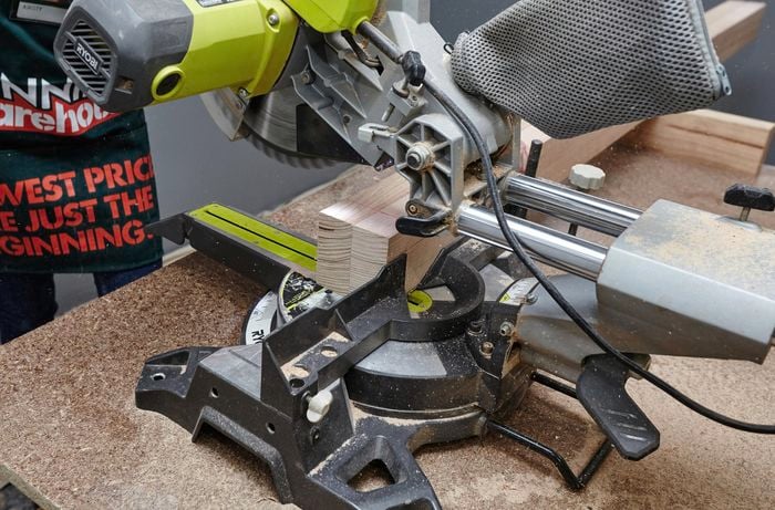 The post of a wooden coat rack being cut to size by a Bunnings staff member with a mitre saw