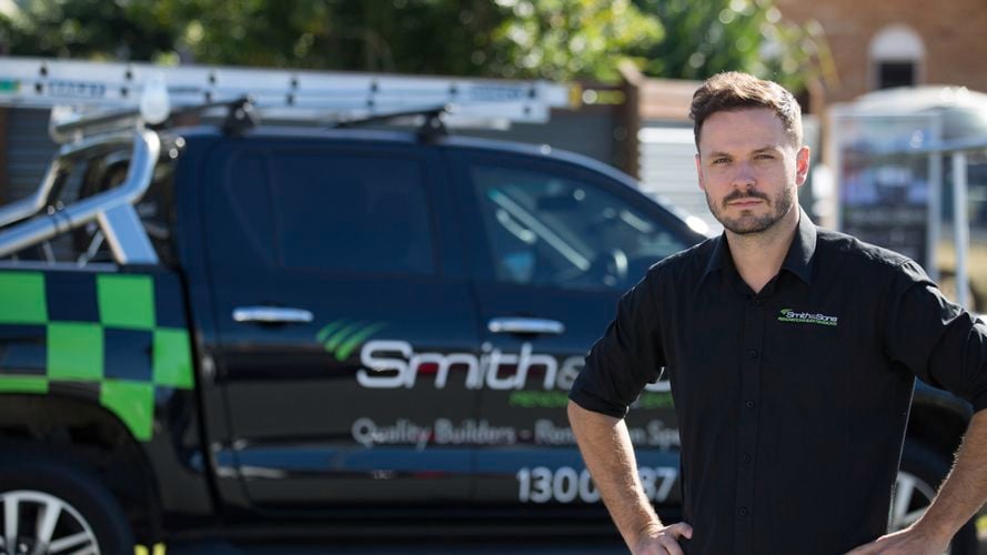 Person standing in front of a Smithers-branded black pickup truck with ladder and green checkered pattern.