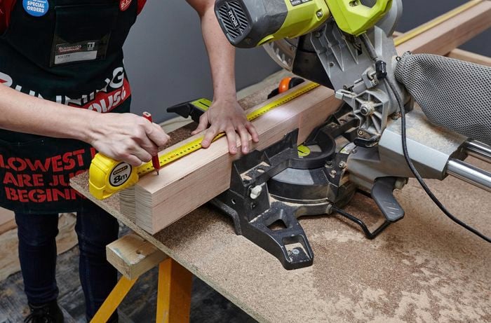 Two pieces of timber underneath a mitre saw being marked for cutting with a pencil and tape measure
