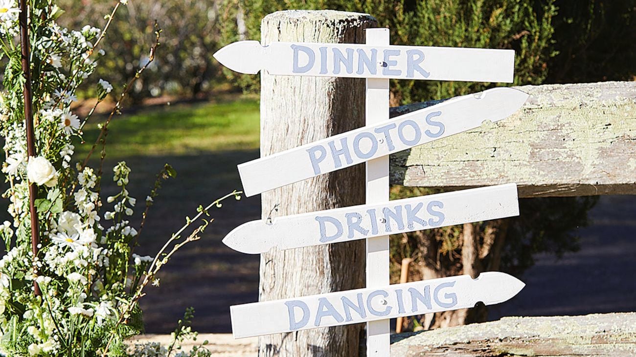 An innovative D.I.Y. sign is made from simple fence pickets. that reads 'dinner, photos, drinks, dancing'.