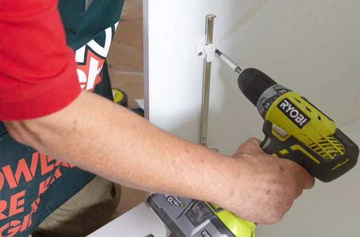 Person drilling door guide piece to linen cupboard panel.