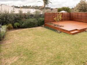 A neatly landscaped backyard features a wooden deck with a small tree