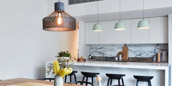 Large pendant light hanging above a dining table with a kitchen in the background and three smaller pendant lights.
