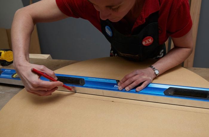 Person measuring and marking timber with level and pencil