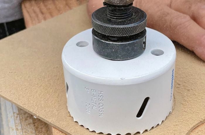 A person using a holesaw to cut an MDF panel to shape.