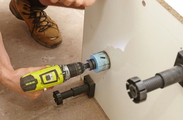 Cutting out a hole for the drain pipe with a drill and hole saw.