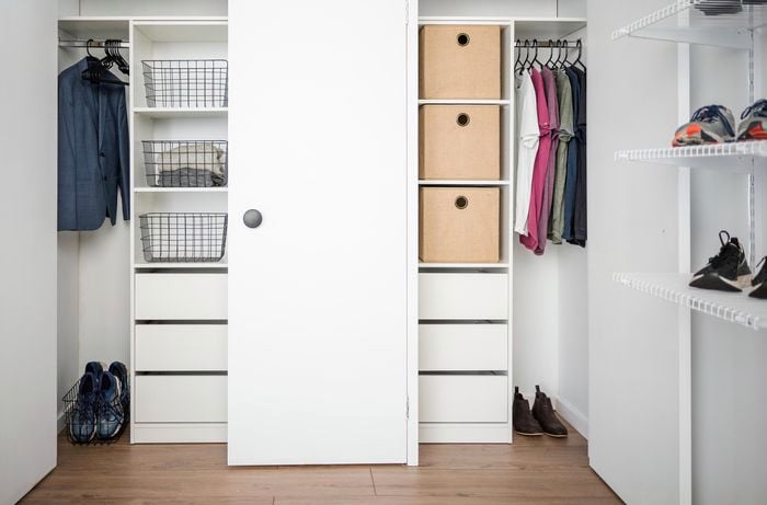A wardrobe with shelves in it with clothes hanging and shoes on them and drawers in it with a timber floow