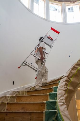 Person carrying ladder under their arm up the stairs