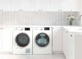 Laundry with white cabinets, white herringbone tiles and washer and dryer.