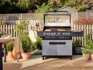 Steel BBQ outside on a timber decking next to a table with crockery on it.