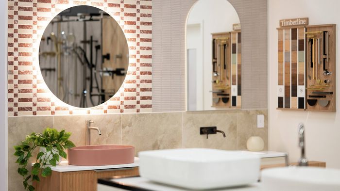 Bathroom showroom display with illuminated mirror, pink basin and tile samples.