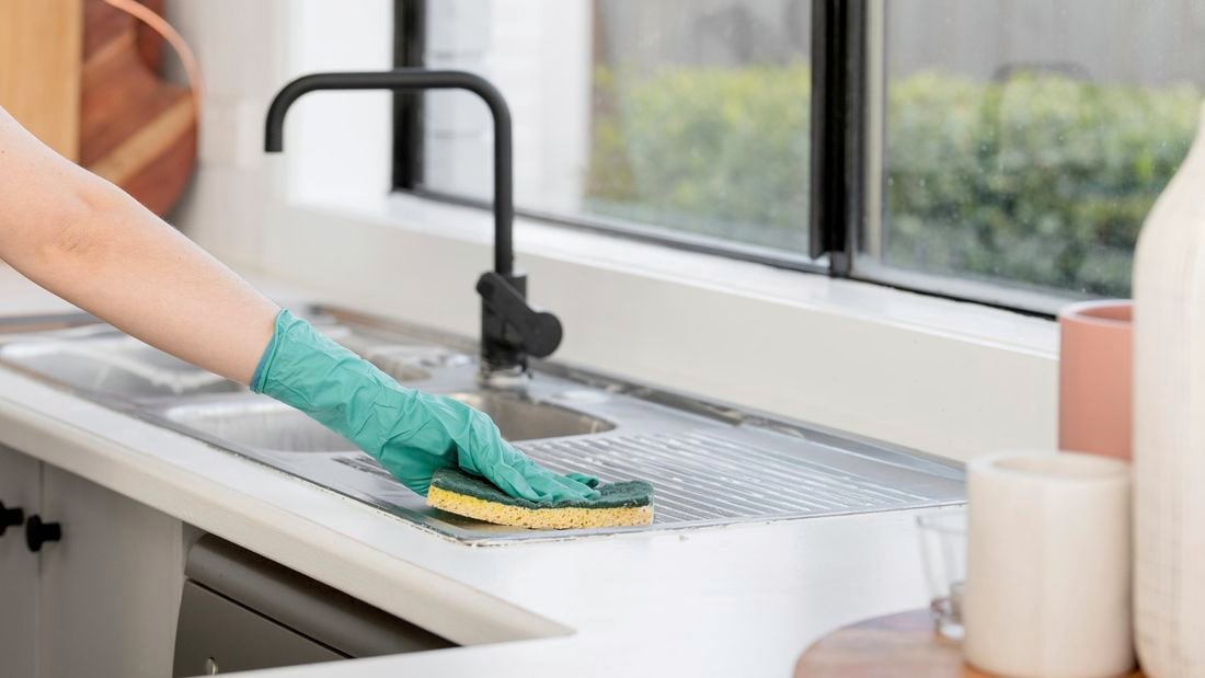 A kitchen sink being wiped clean with a sponge