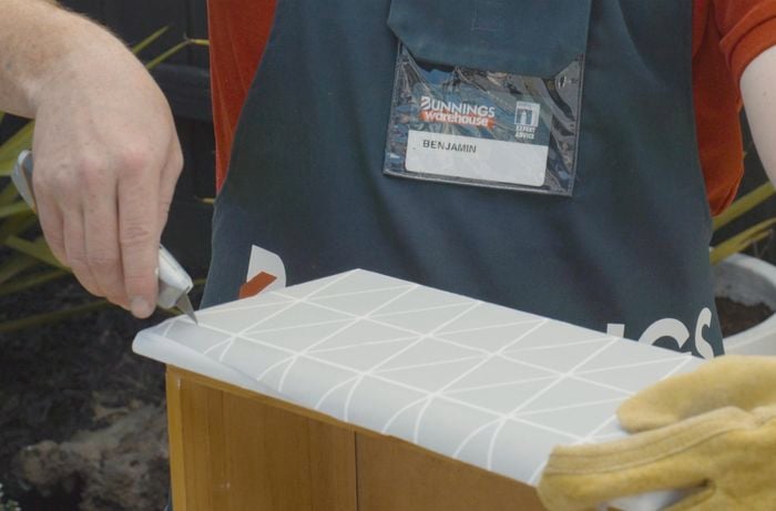 Person cutting wallpaper on the front of a drawer with a utility knife