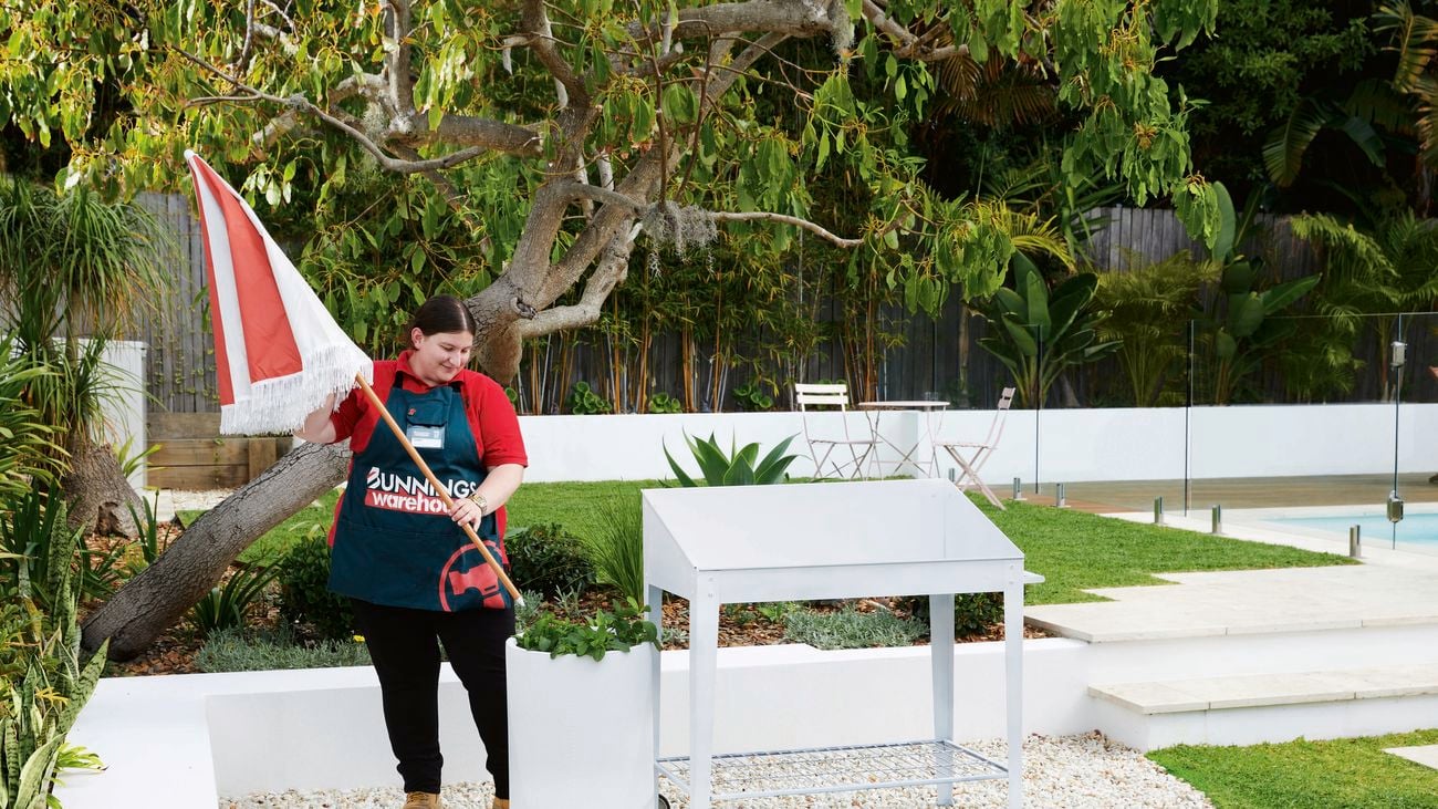 Bunnings employee puts a large, red and white umbrella into a pot plant next to a white drinks trolley.