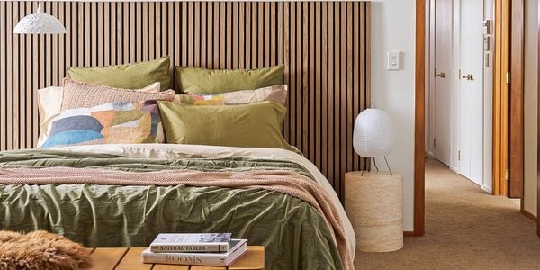 A bedroom showing a bed with a timber headboard, cosy blankets and pillows to help with home insulation