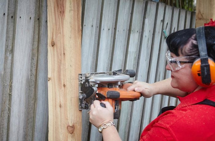 A person wearing protective gear cutting into a fence post using a circular saw