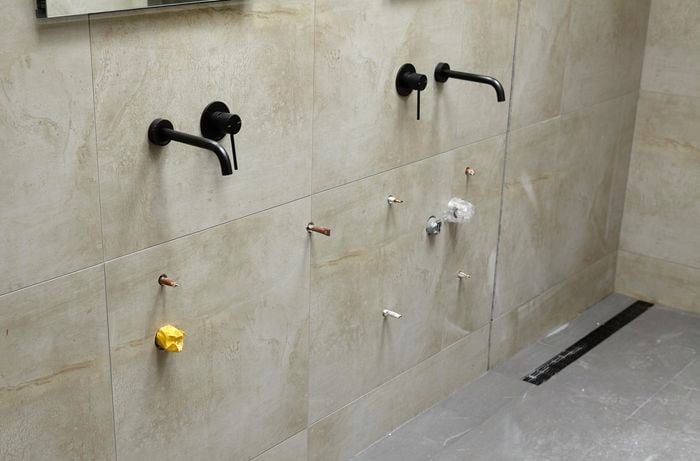 A bathroom wall with pipes protruding through holes in the tiles