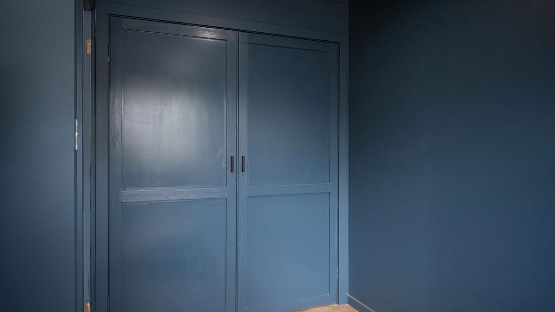 Image of a wardrobe with two doors, painted in a deep shade of navy blue, with a smooth and glossy finish.