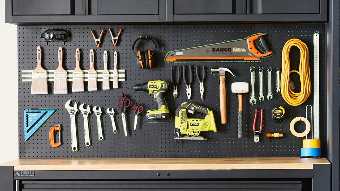 A black wall-mounted pegboard with neatly hanging tools, paintbrushes, cables and headphones.