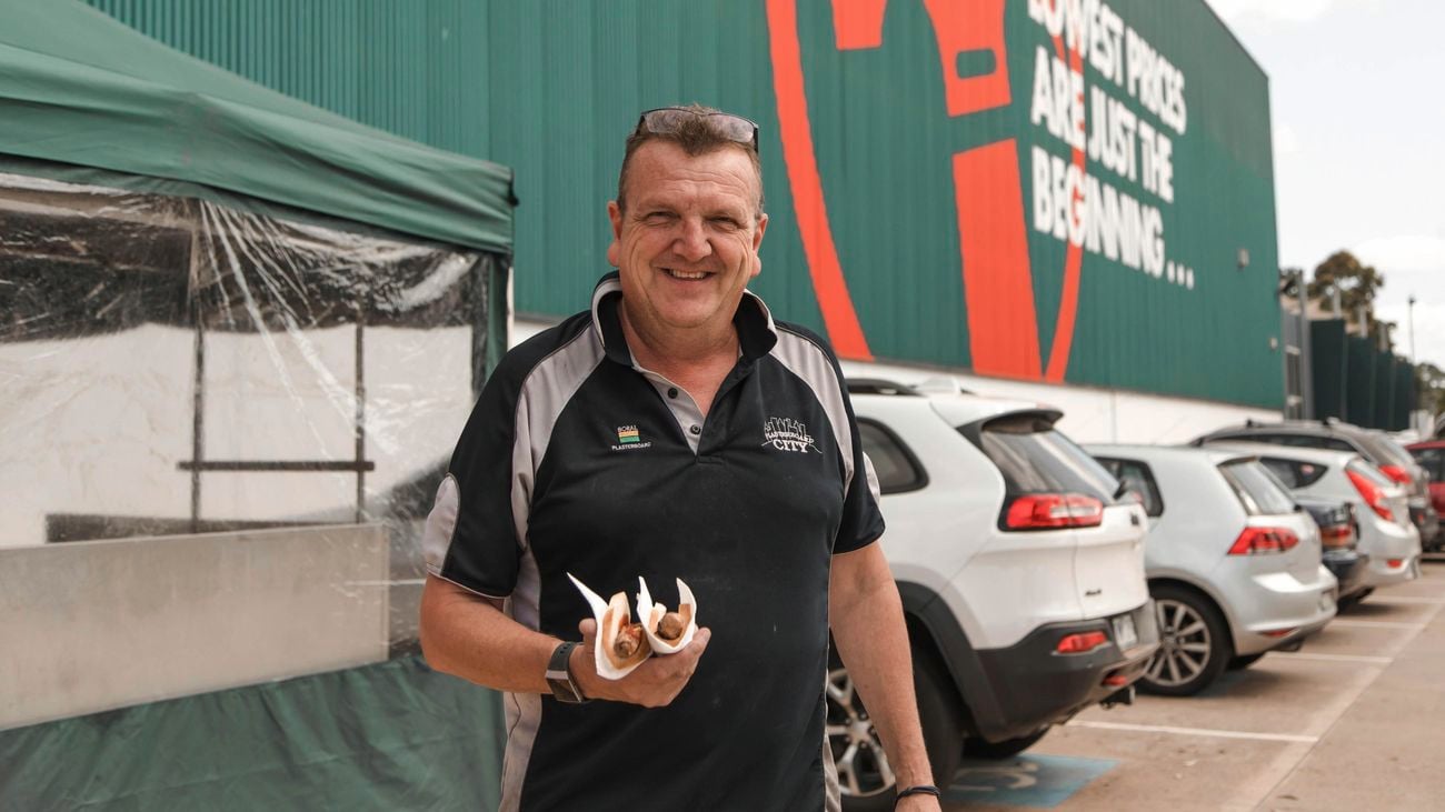 A person holding a sausage in bread out the front of a Bunnings store