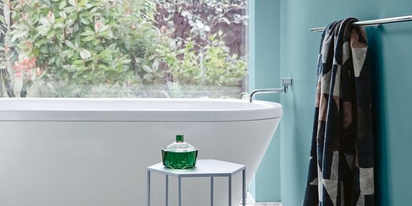 A bathroom with soft green feature wall, white bath, towel rail and small tool next to bath.